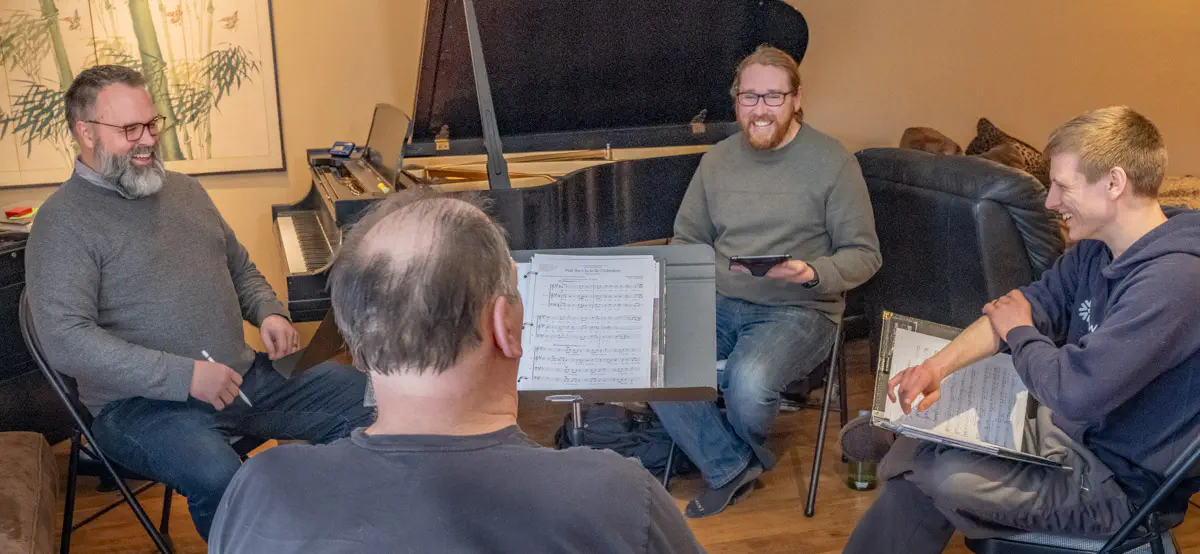 Kaleidoscope Quartet sitting in a circle facing each other with their music in front of them, laughing